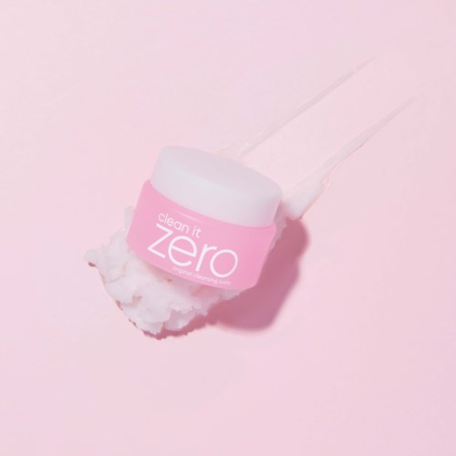 Ein pinker Behälter mit 'clean it zero' auf einer rosa Oberfläche, mit Wattepad und Creme.
