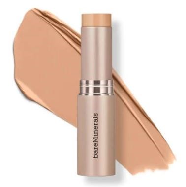 En beige makeup-sticka med en silverring, ligger på ett beige prov. Märket är BareMinerals.