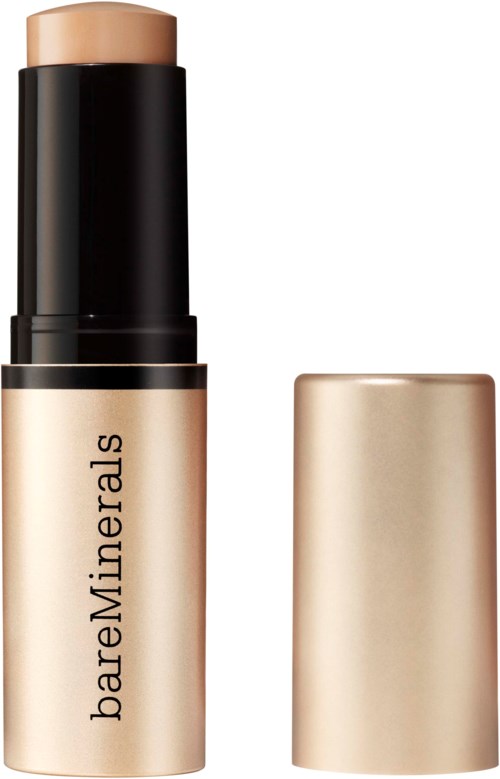 Ett stiftgrundläggningsprodukt med guldfärg och svart förpackning, märkt BareMinerals, och korken är borttagen.