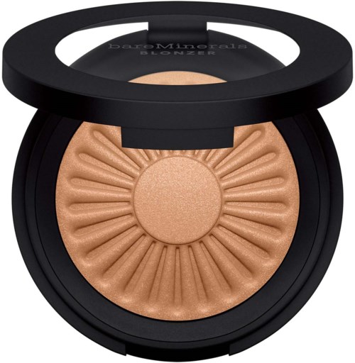 A round makeup compact with a light beige or peach-colored powder and a decorative sunburst pattern. The lid is open.