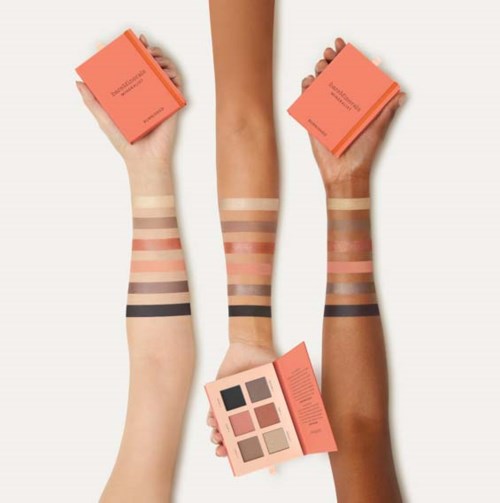 Tre armar visar olika makeupprov och rosa makeuppaket, med en arm som håller en ögonskuggspalett.