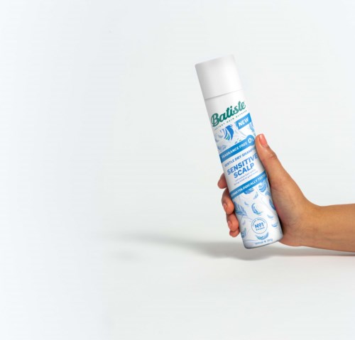Een hand houdt een busje Batiste droogshampoo tegen een witte achtergrond.