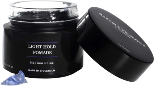 A black jar labeled 'Light Hold Pomade, Medium Shine' with a lid and a small amount of blue product outside.