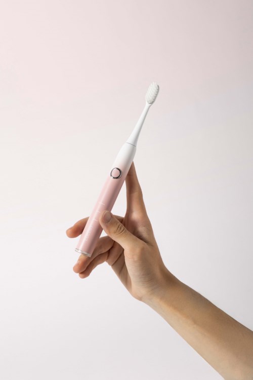 A hand holds a pink electric toothbrush against a plain light background.