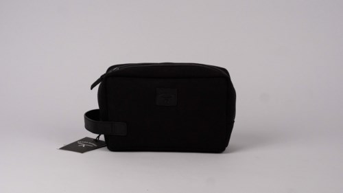 A small black bag with a handle, zipper, and a tag attached, placed on a plain white surface.