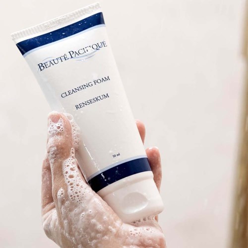 Een hand houdt een tube met reinigingsschuim met de tekst 'Beaute Pacifique'. Het schuim is zeepachtig en gedeeltelijk bedekt de hand.