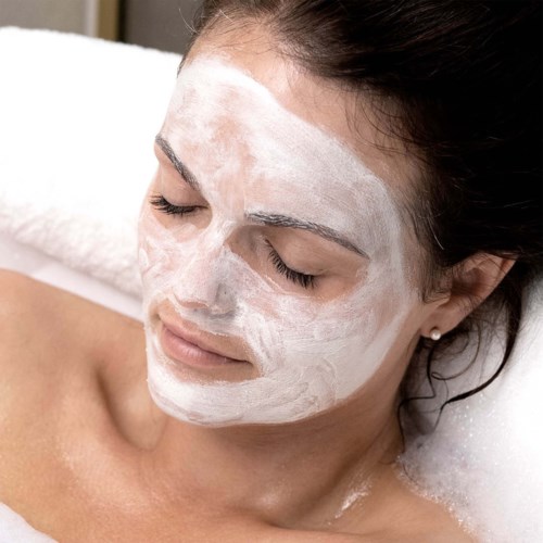 Een vrouw ontspant met een gezichtsmasker, ligt met gesloten ogen en geniet van een huidverzorgingsbehandeling.