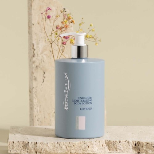A light blue bottle of moisturizing body lotion with a pump, placed on a stone surface, with dried flowers in background.