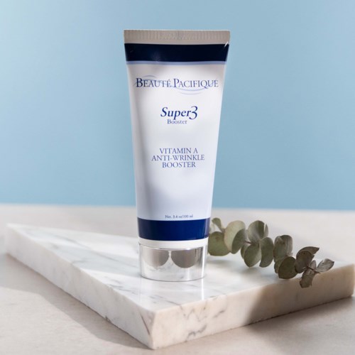 Een witte en blauwe tube met de tekst 'Super 3 Booster' en 'Vitamin A Anti-Wrinkle'. Het staat op een witte marmeren plaat met eucalyptusbladeren.