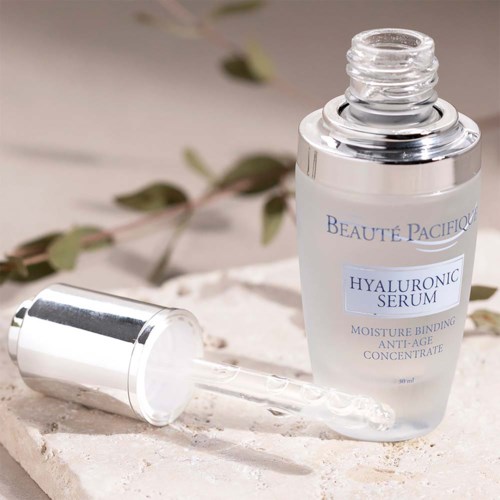 Hyaluronsäure-Serumflasche mit Pipette offen, auf einem Steintisch mit Pflanze im Hintergrund.