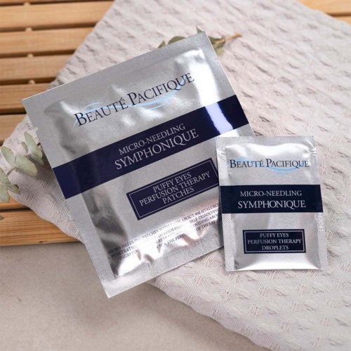Twee zilveren zakjes van Beauté Pacifique micro-needling patches op een wit doek met houten achtergrond.
