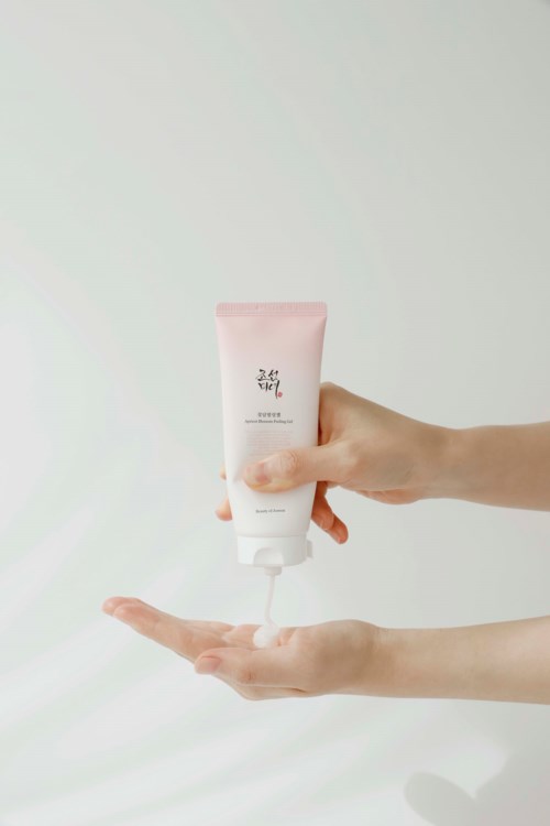 A person squeezes a pink and white tube of cream or lotion over their open palm.