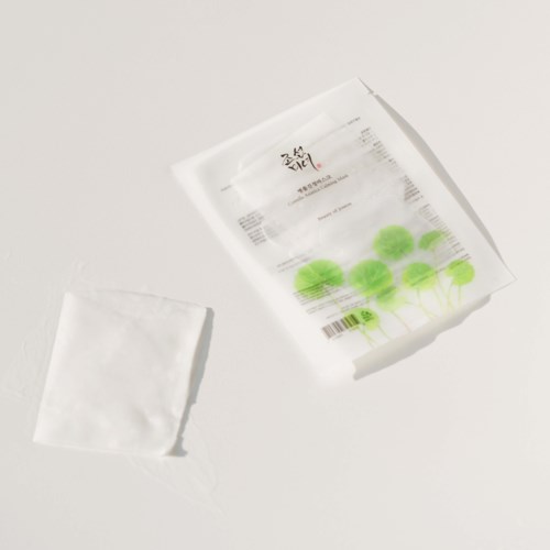 A white paper bag with green circles, and a small white cloth or paper, on a white surface.