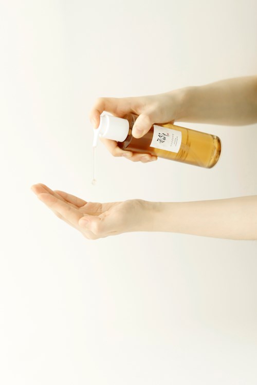 Eine Person gießt Lotion oder Flüssigkeit aus einer kleinen Flasche in die Hand gegen einen schlichten Hintergrund.