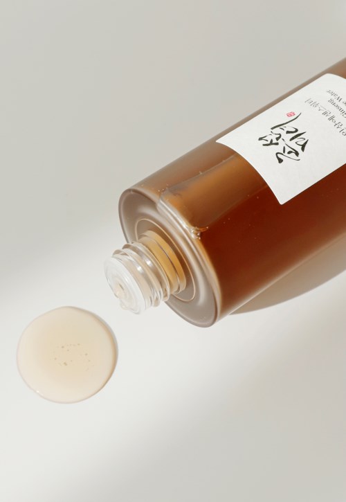 Eine braune Flasche neigt sich, mit Creme oder Lotion, die auf eine weiße Oberfläche tropft.