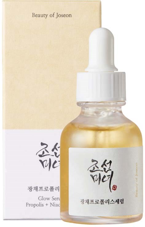A small dropper bottle labeled in Korean, with a beige box behind it, indicating skincare product with gold liquid inside.