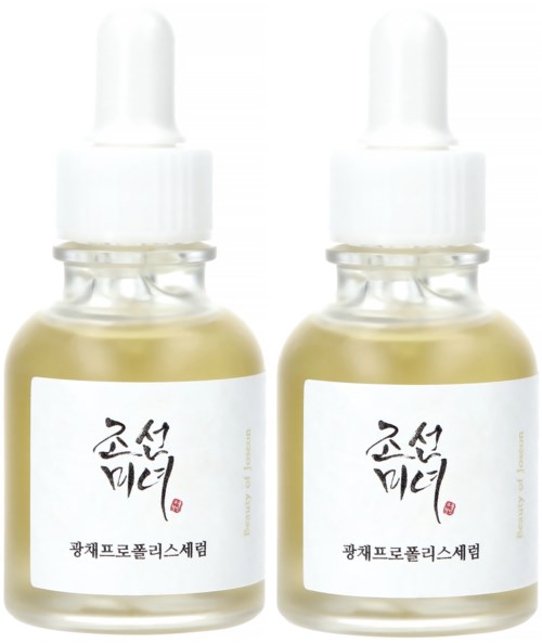 Twee kleine flesjes serum met witte labels en druppelaars, gevuld met lichtgele vloeistof.
