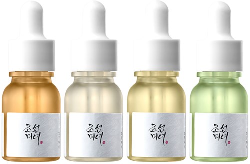 Vier kleine flessen met huidverzorgingsproducten in verschillende kleuren met witte druppels. Elke fles heeft een wit label met zwarte tekst.