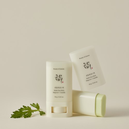 Two skincare containers, one lying down and one standing, with a green leaf beside them, on a plain background.