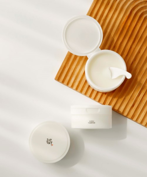 A white jar with a spoon, a closed jar with Asian characters, and a wooden mat on a white surface.