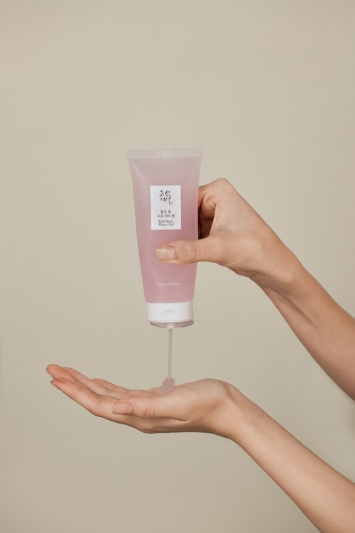 Een persoon houdt een roze tube en drukt wat product in zijn open hand.
