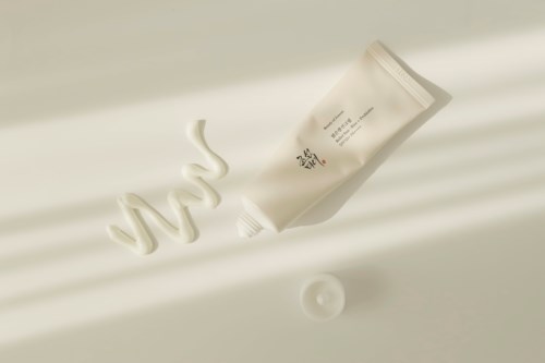 A white tube with Korean text, some cream swirl, and a small round blob on a light surface.