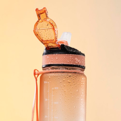En rosa proteinshakeflaske med svart lokk, åpen topp med en skei inni, vanndråper på overflaten.
