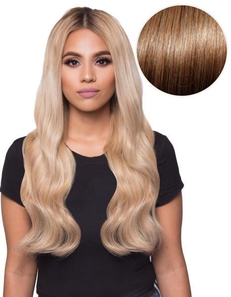 Eine Frau mit langen, gewellten blonden Haaren, in einem schwarzen Hemd, Portrait vor hellem Hintergrund.