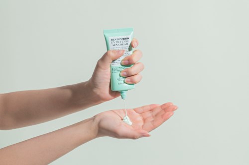 Iemand knijpt crème uit een tube op hun hand, met een eenvoudige achtergrond.