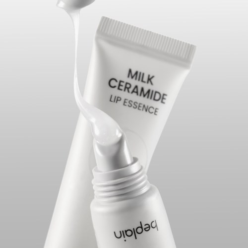 Een witte tube met de tekst 'Milk Ceramide Lip Essence' en een druppel vloeistof die eruit komt. De tube is open en lekt.