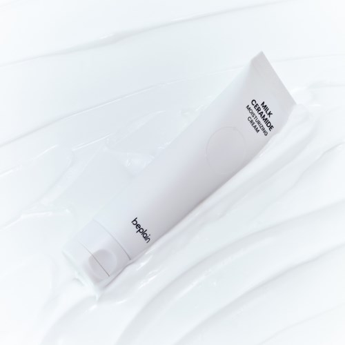 Een witte tube met het label 'milk ceramide calming mask' ligt op een witte ondergrond.