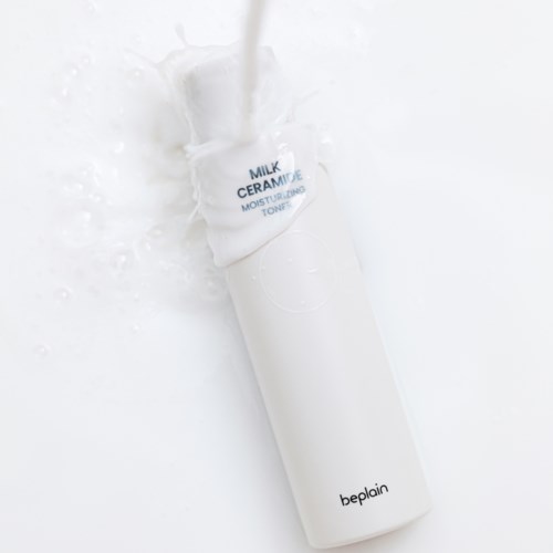 Een witte cilindervormige fles met label 'Milk Ceramic Moisturizing Toner' wordt met water overgieten.
