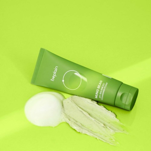 Grüne Tube mit Hautcreme, Schaum und Creme auf grünem Hintergrund.