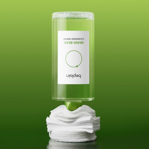 A clear green bottle labeled 'Mungo Green' upside down with a neat stack of cotton pads below it.