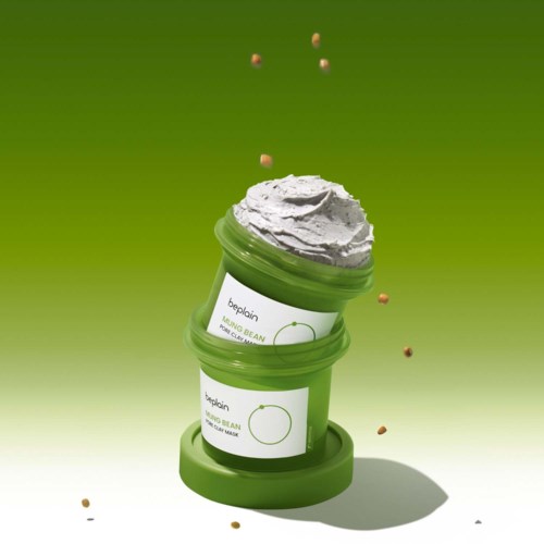 Twee groene potjes met bonenpuree met slagroom, gestapeld met kleine verspreide zaden of graan, op een groene achtergrond.