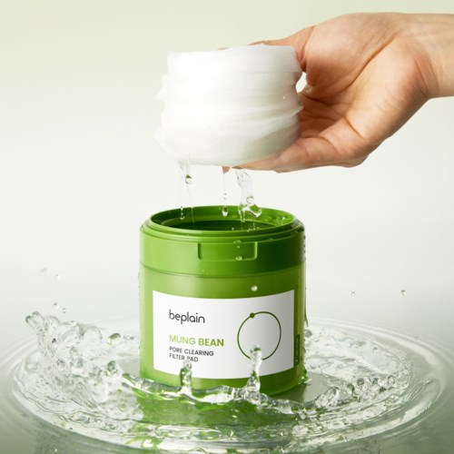 Een hand houdt een ronde witte spons boven een groene container met filterpads, water spettert.