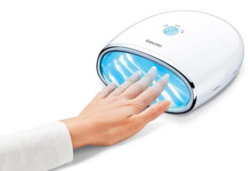 Een hand is geplaatst in een witte, ovale UV-nagellamp met blauwe gloed.