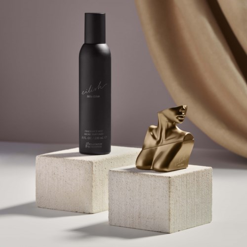 Een zwarte fles met sierlijke tekst naast een gouden abstract beeld op witte blokken.