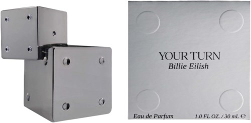 Een zilverkleurige parfumdoos en een wit boekje met zwarte tekst, inclusief de naam Billie Eilish en parfumdetails.