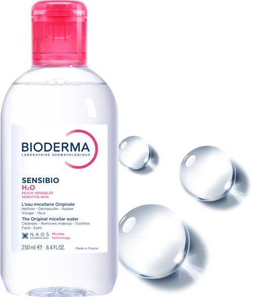 A bottle of Bioderma Sensibio H2O micellar water, with three drops nearby, labeled for sensitive skin.
