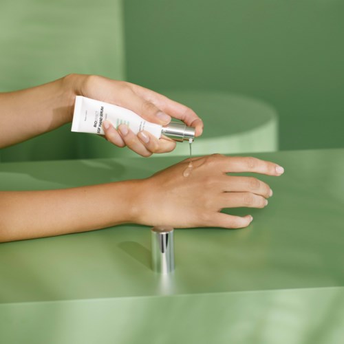 A person applying lotion or cream to their arm over a green surface.