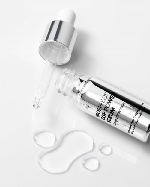 A small bottle of serum with a dropper cap, some serum drops and a wound healing label on white background.
