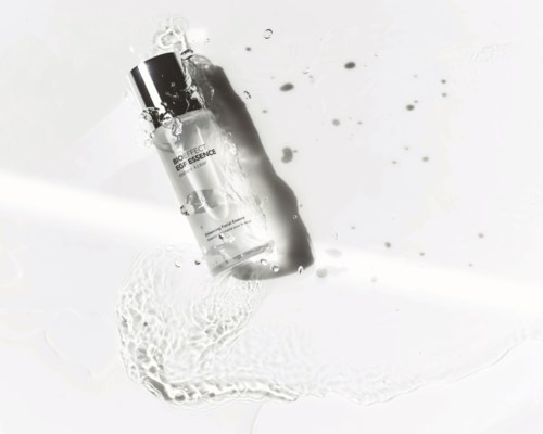 A skincare bottle with water splashing around it, placed on a light surface in a minimal style.