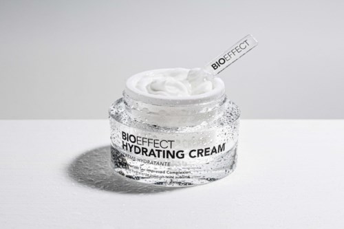 A clear jar of hydrating cream with a label, open lid, and cream inside, placed on a white surface.