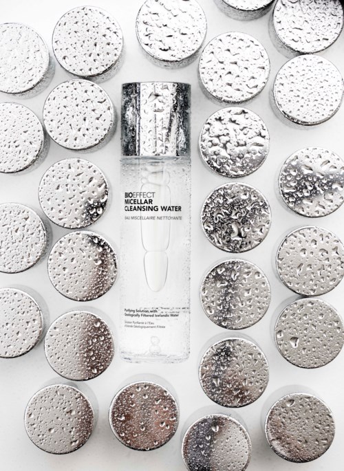 A clear bottle of cleansing water surrounded by numerous round, textured mirrors with water droplets on them.