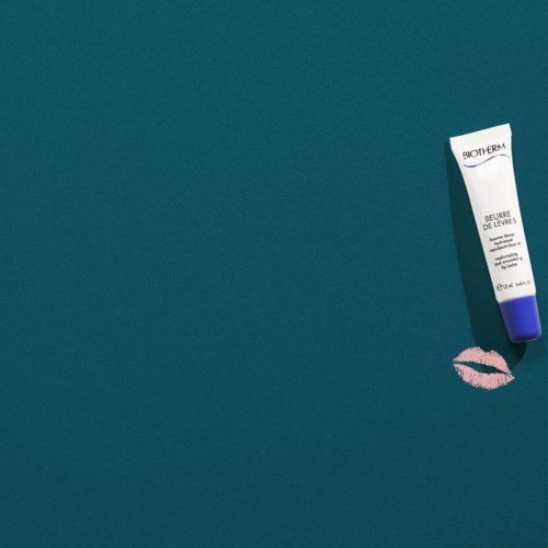 Een tube Biotherm lippenbalsem en een roze lipafdruk op een blauwe achtergrond.