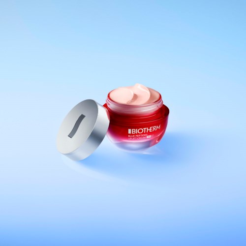 A red jar of cream with a silver lid open, placed on a light blue background.
