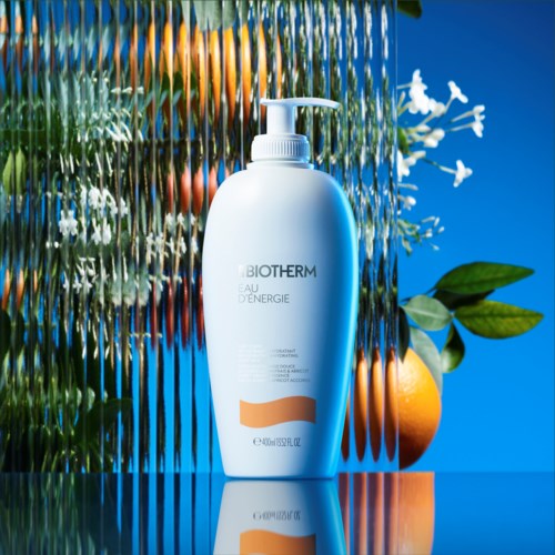 Een witte Biotherm huidverzorgingsfles met pomp, omgeven door blauwe achtergrond en groen, met fruit en planten.