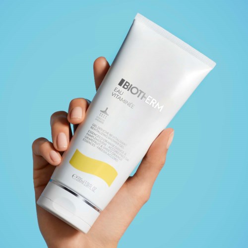 Een hand houdt een witte tube van Biotherm skincare-crème tegen een lichtblauwe achtergrond.