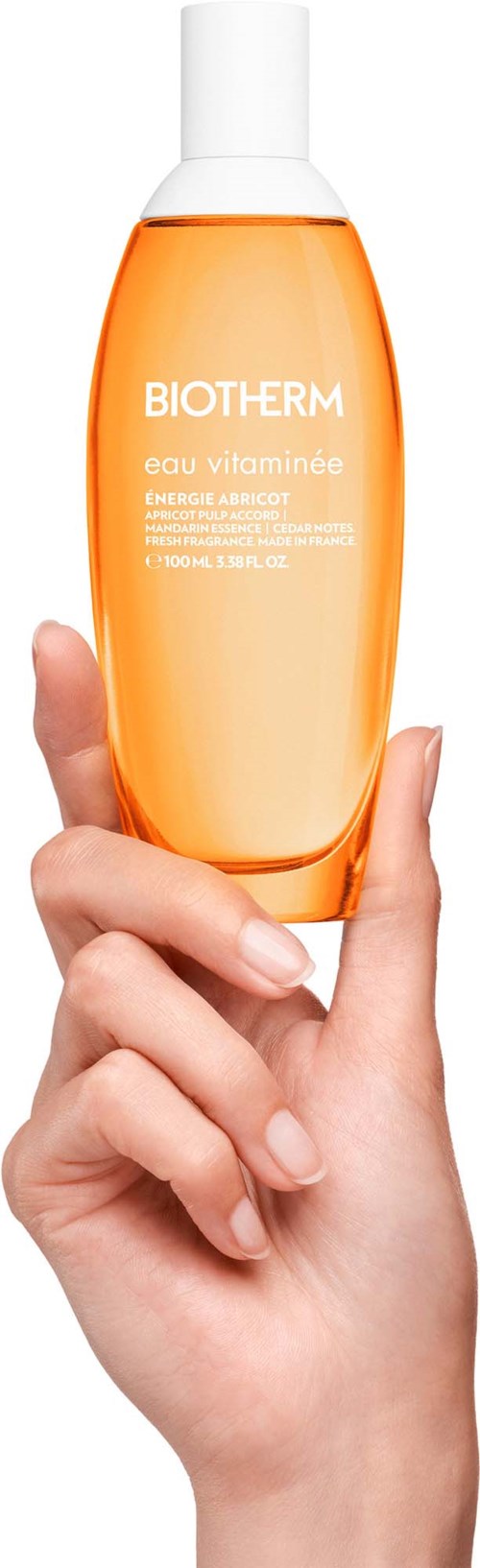 Eine Hand hält eine orange Flasche mit weißem Deckel von Biotherm, mit klarer Beschriftung, vor weißem Hintergrund.